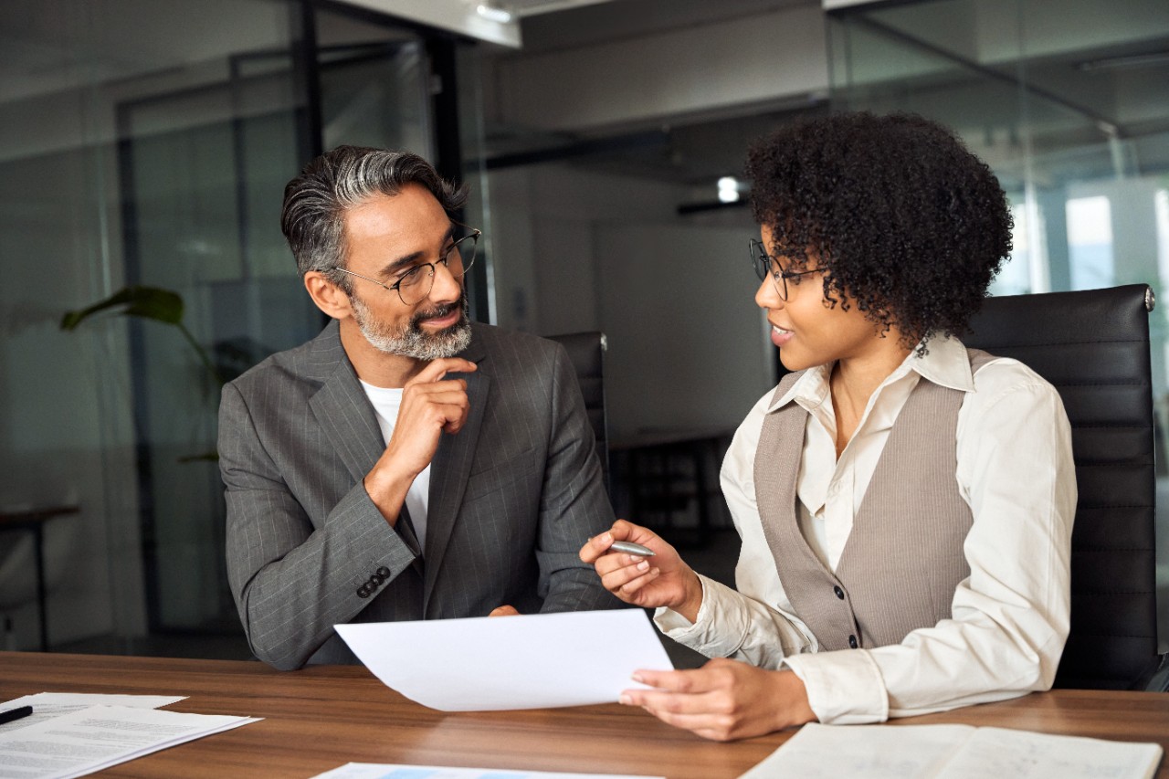 African female financial advisor consulting client investor reading document.
